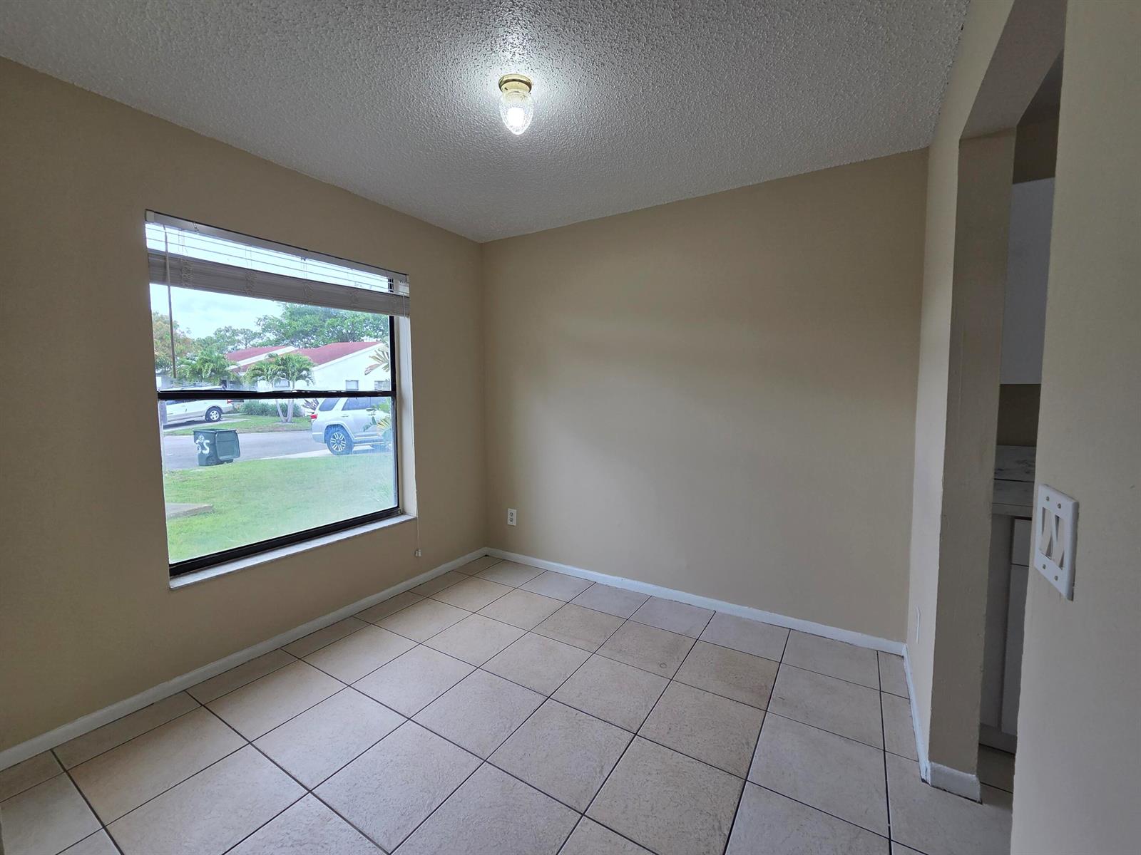 An empty room with beige walls, tile flooring, a large window, and a ceiling light — 3774 Mil Race Court, FL 33463, FL
