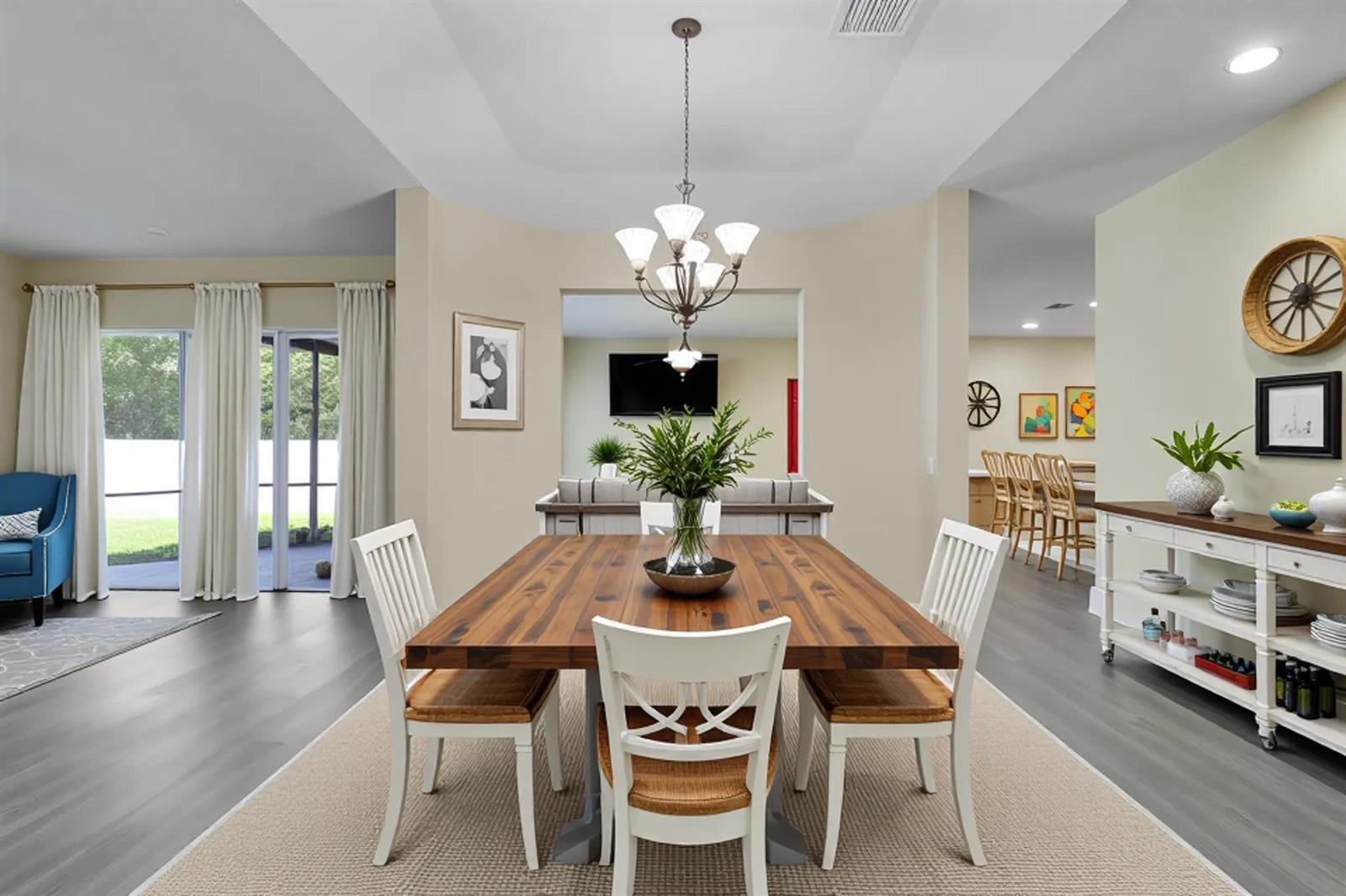 A dining room features a wooden table, white chairs, and a chandelier on gray flooring — 10075 Freesian Way, Lake Worth FL 33449, LAKE WORTH, FL