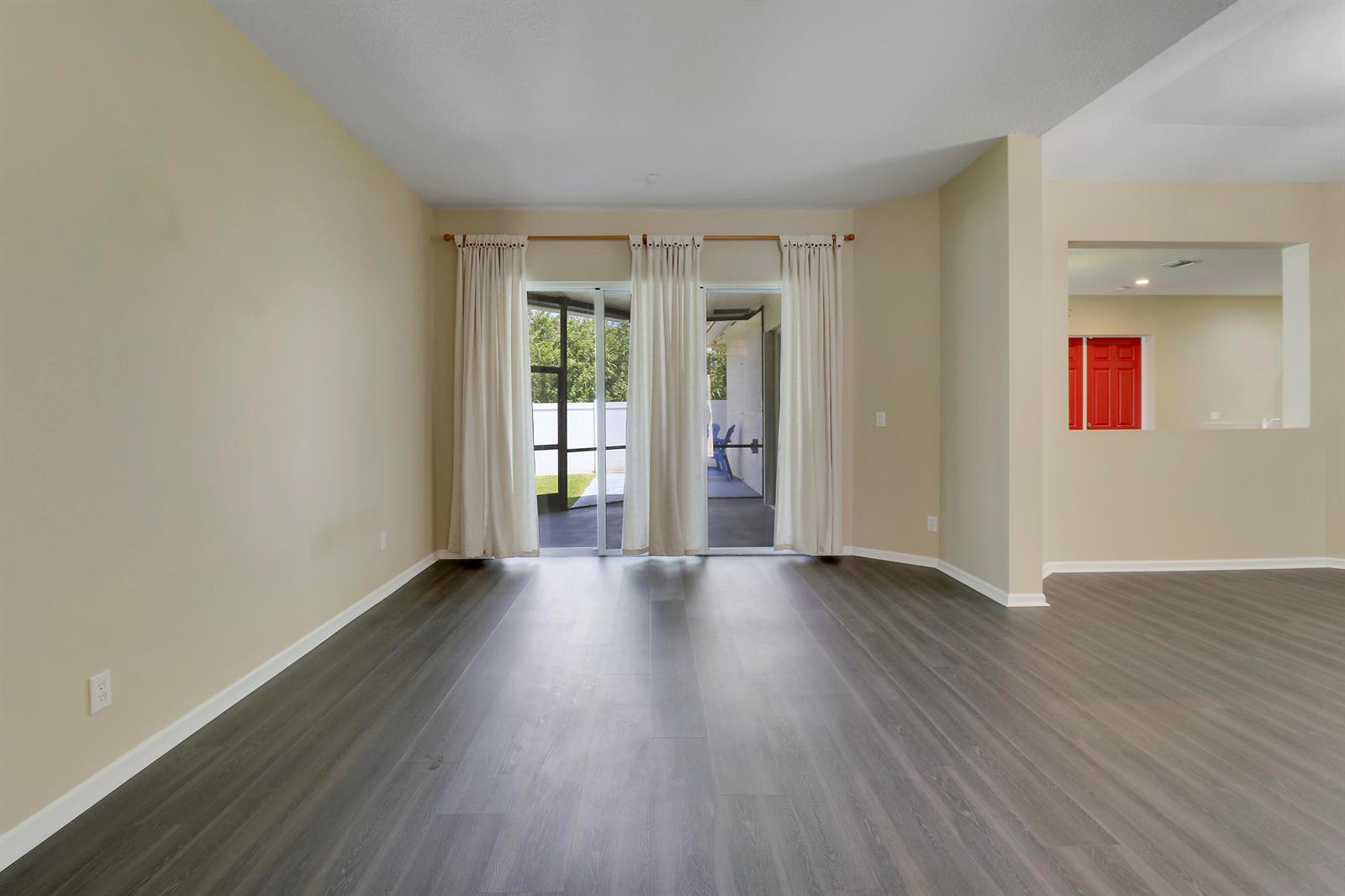 An empty room with wood-look flooring, beige walls, and sliding glass doors leading to a patio — 10075 Freesian Way, Lake Worth FL 33449, LAKE WORTH, FL