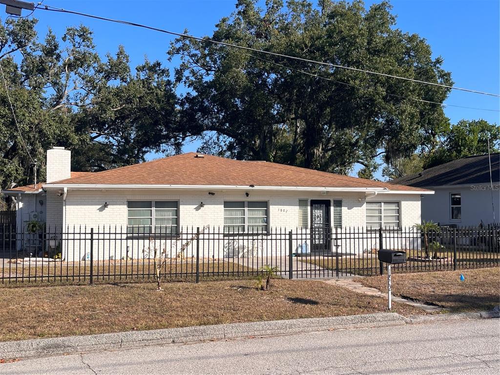 A single-story white brick house with a brown shingled roof sits behind a black fence — 1802 E KNOLLWOOD STREET, TAMPA, FL