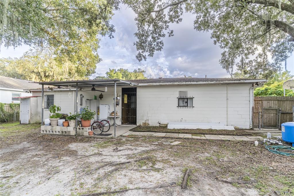 A white concrete block house with a metal patio cover sits next to a large tree — 1802 E KNOLLWOOD STREET, TAMPA, FL