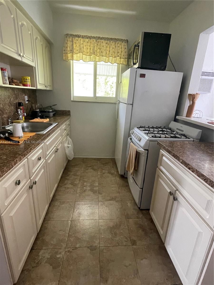 A narrow kitchen features white cabinets, a gas stove, and brown tile flooring — 1000 Biarritz Dr # 3, Miami Beach FL 33141, MIAMI BEACH, FL