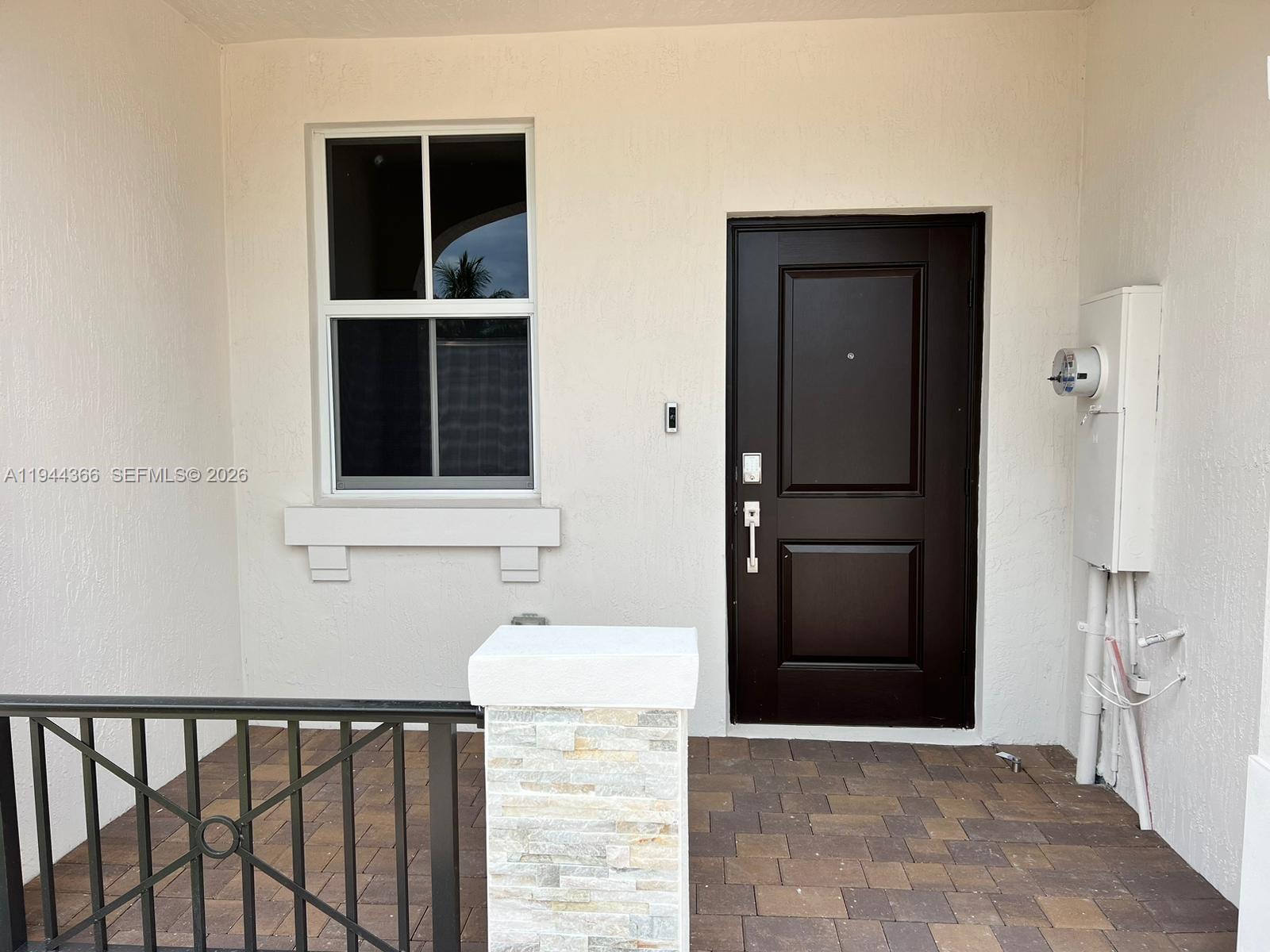 A dark brown front door sits next to a window on a paved porch — 12560 NW 22nd Pl, Miami FL 33167, MIAMI, FL