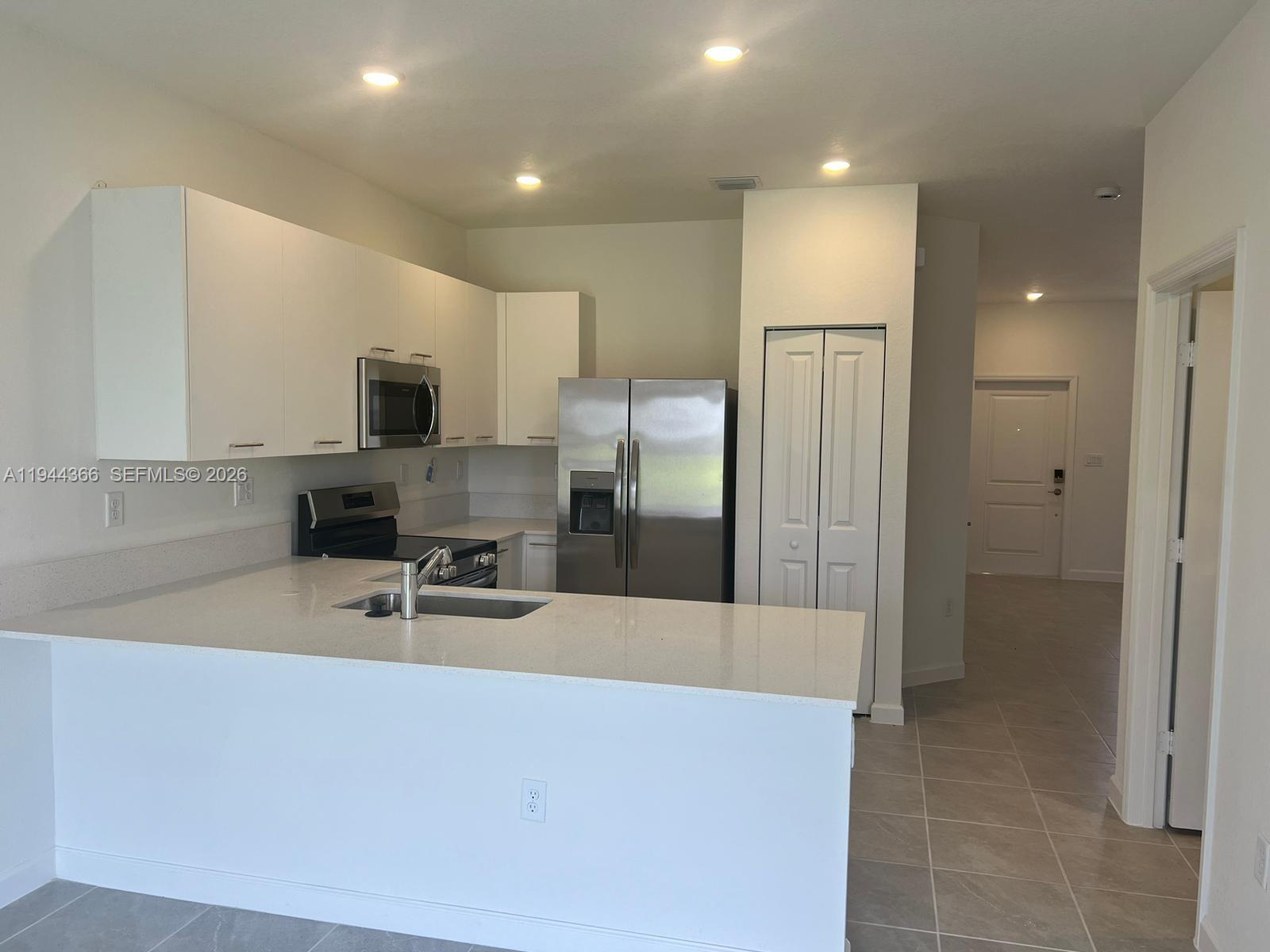 A kitchen features white cabinets, stainless steel appliances, and a peninsula with a sink — 12560 NW 22nd Pl, Miami FL 33167, MIAMI, FL