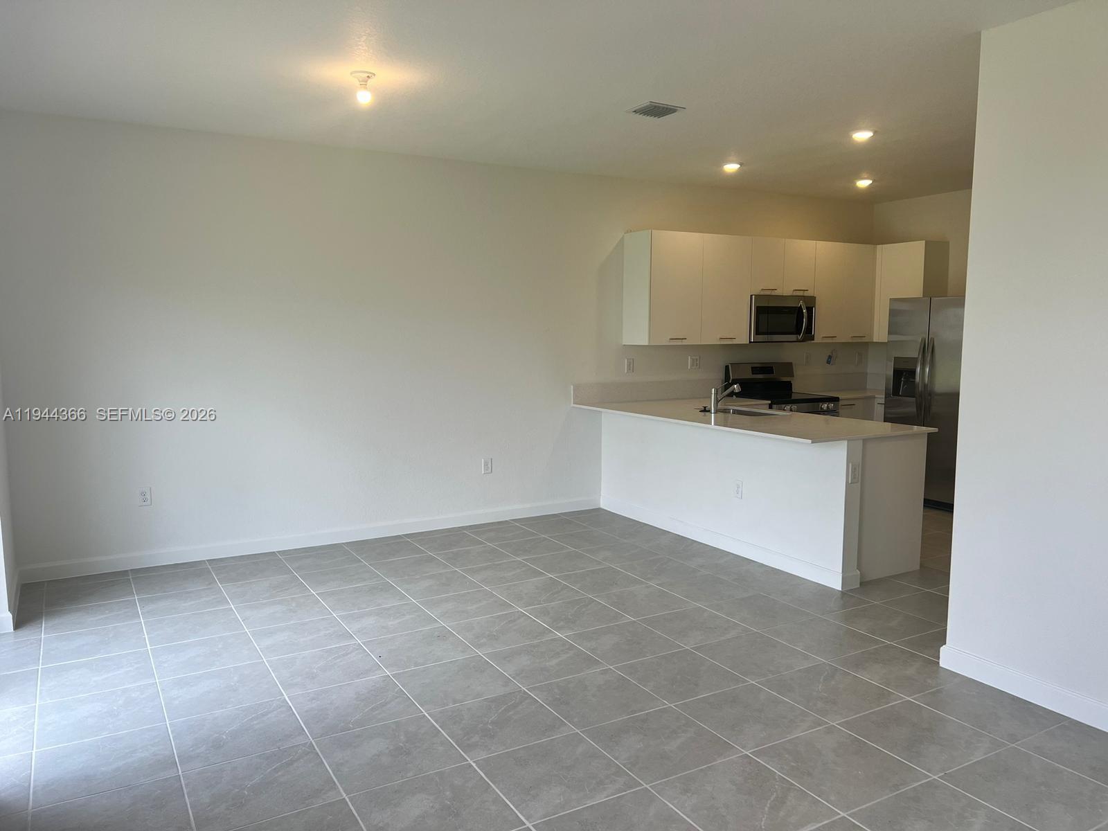 An open-concept kitchen features white cabinets, stainless steel appliances, and gray tile flooring — 12560 NW 22nd Pl, Miami FL 33167, MIAMI, FL