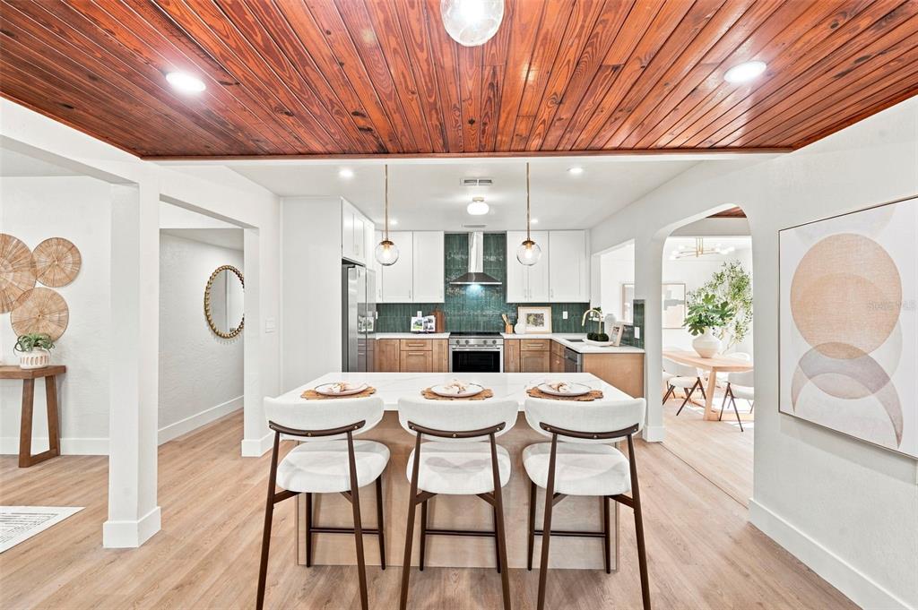 A kitchen features a wood-paneled ceiling, a central island with three stools, and white cabinetry — 7326 11TH AVENUE N, ST PETERSBURG, FL