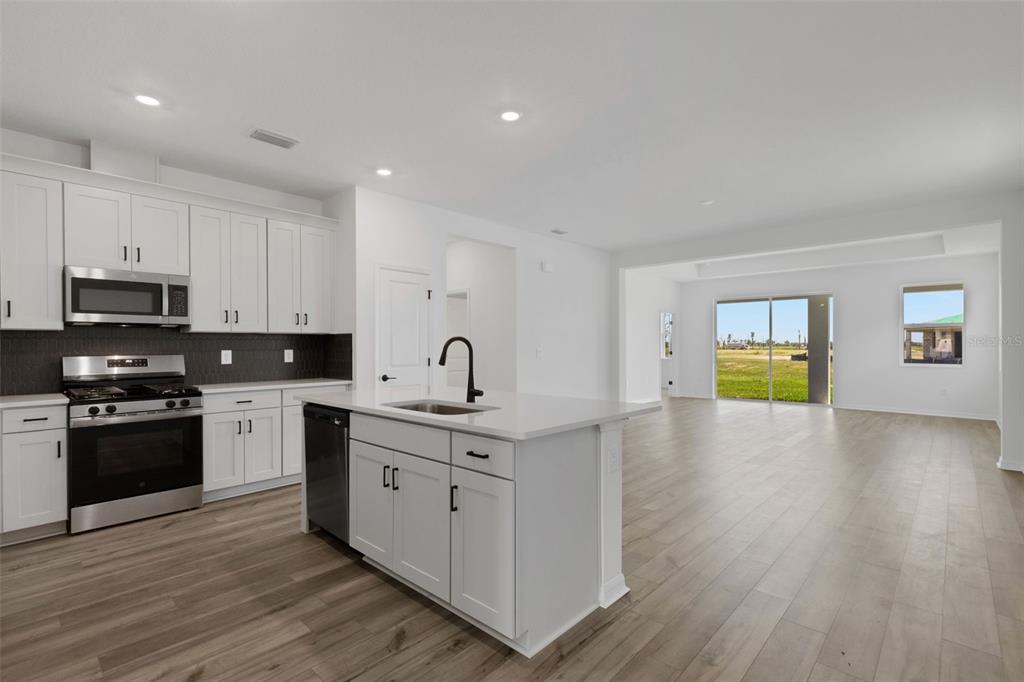 A modern kitchen with white cabinets and a central island opens into a spacious living area — 8717 CANARD CV, PALMETTO, FL