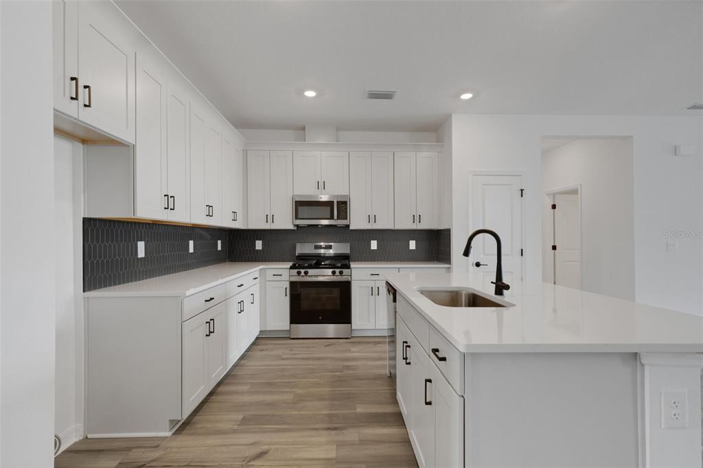 A modern kitchen features white cabinets, stainless steel appliances, a dark backsplash, and a central island — 8717 CANARD CV, PALMETTO, FL
