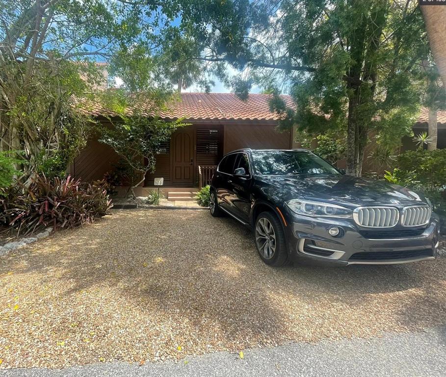A dark SUV is parked on a gravel driveway in front of a brown house — 109 PASS KEY ROAD UNIT 109, SARASOTA, FL