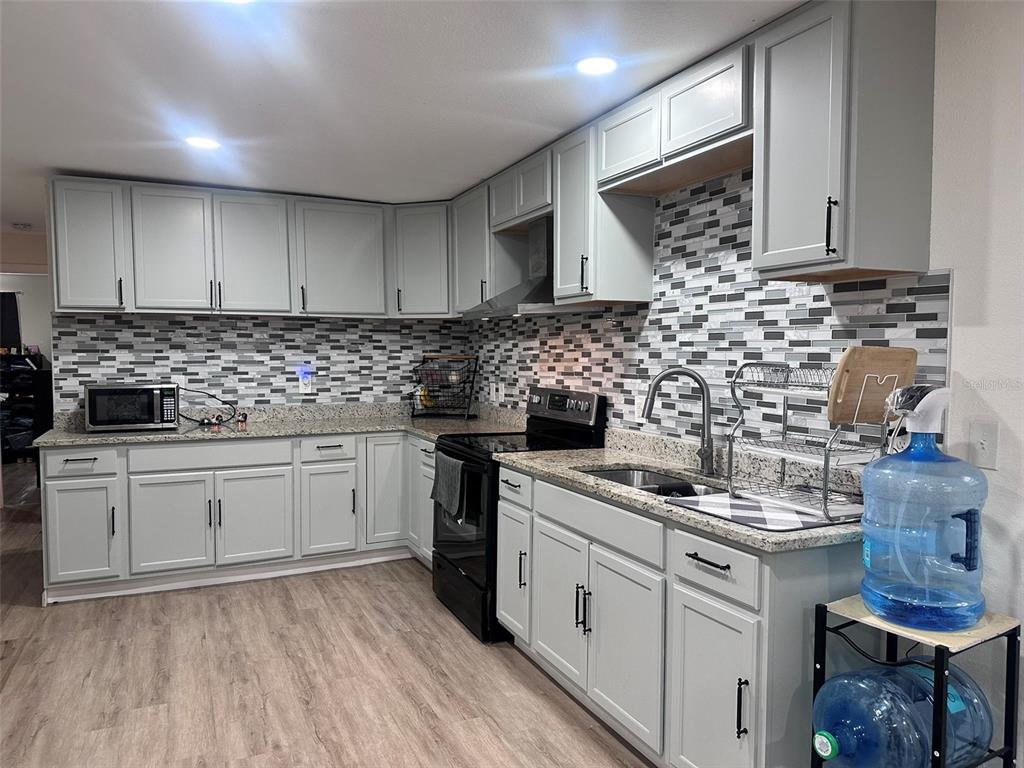 A kitchen features light gray cabinets, granite countertops, a mosaic tile backsplash, and black appliances — 6606 CORBIN LANE, NEW PORT RICHEY, FL