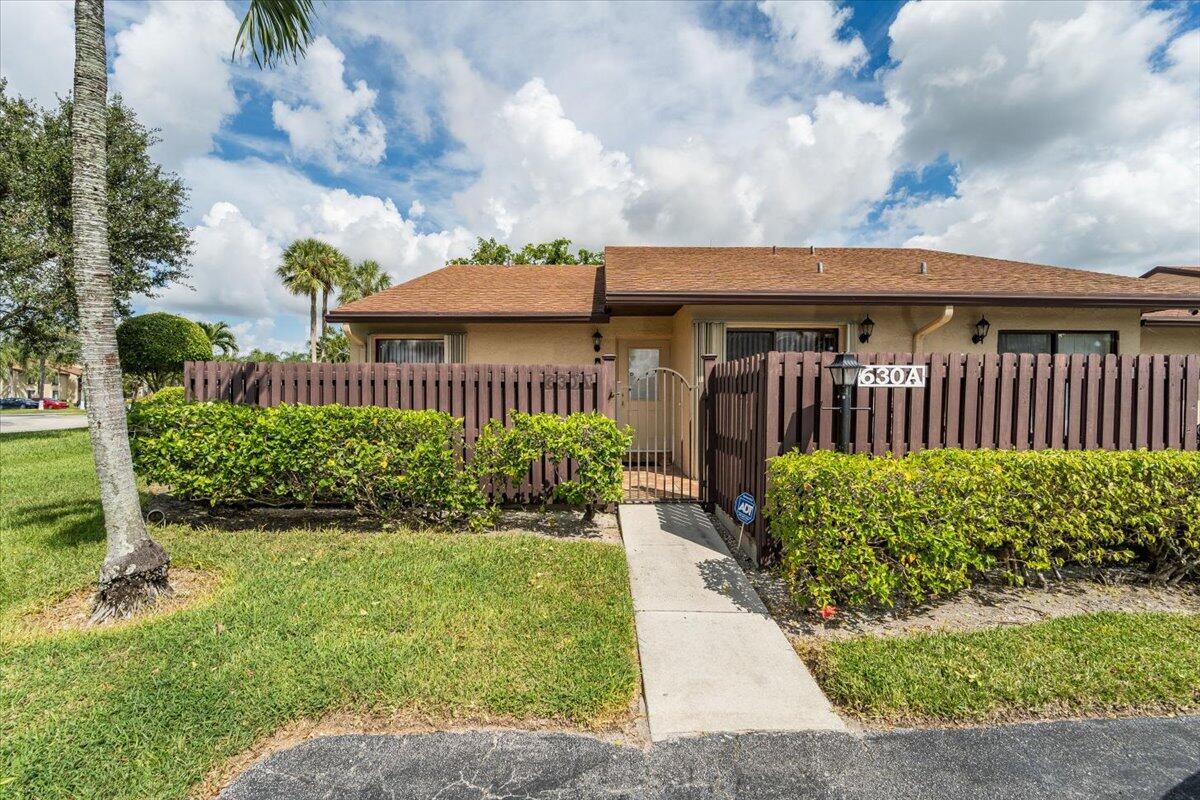 A single-story residential unit features a brown fence, a gated walkway, and a shingled roof — 630 Sea Pine Way # A, FL 33415, FL