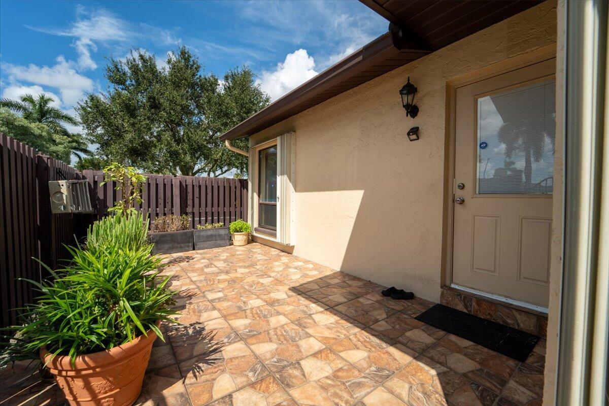 A tiled patio area features a beige exterior wall, a door, and a potted plant — 630 Sea Pine Way # A, FL 33415, FL