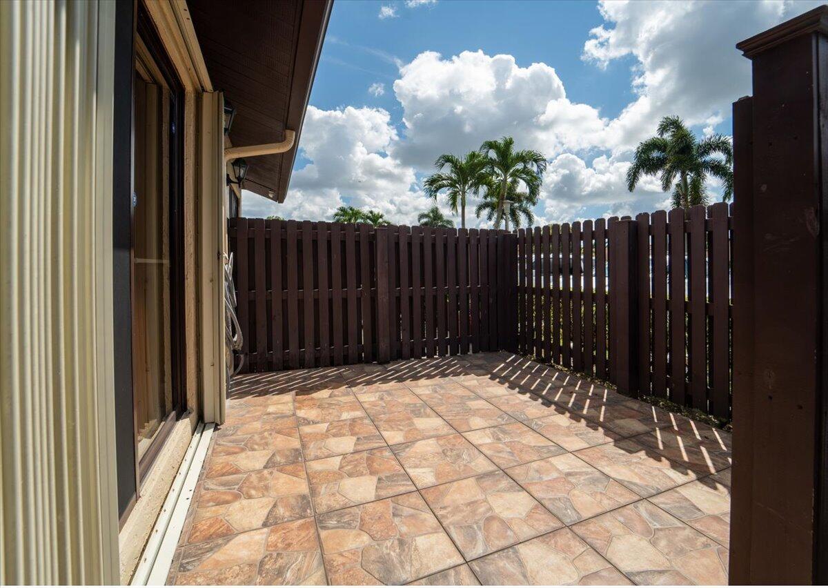 A private patio with stone-look tile flooring enclosed by a dark wood privacy fence — 630 Sea Pine Way # A, FL 33415, FL