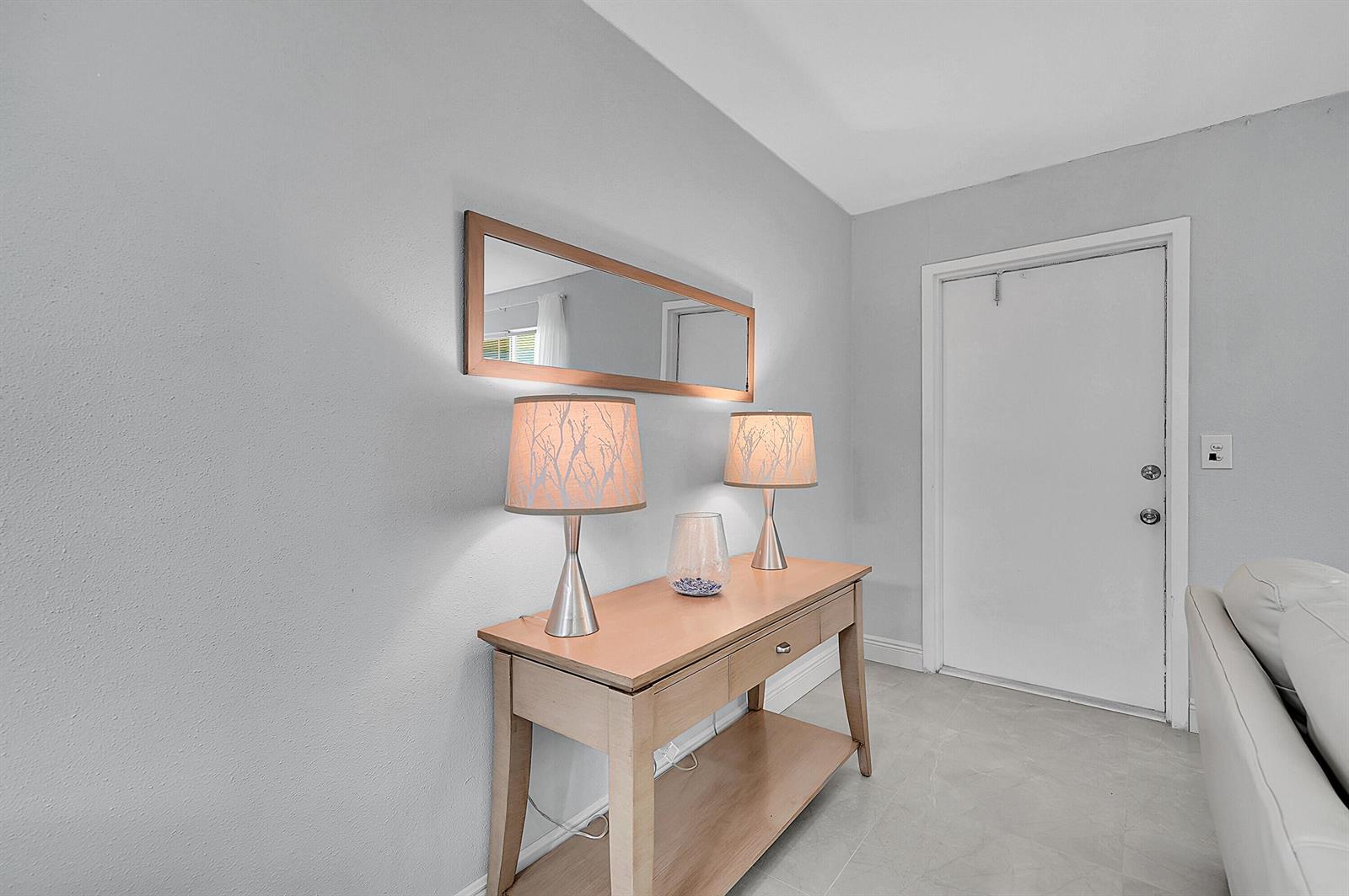 A light-colored entryway features a wooden console table with two lamps and a wall mirror — 646 Flanders N, Delray Beach FL 33484, DELRAY BEACH, FL