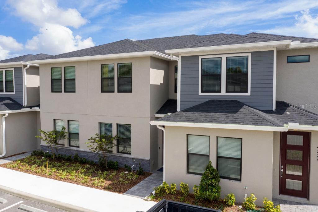 A two-story townhouse exterior features beige stucco, grey siding, a dark roof, and a red door — 4711 TERRA ESMERALDA DRIVE, KISSIMMEE, FL