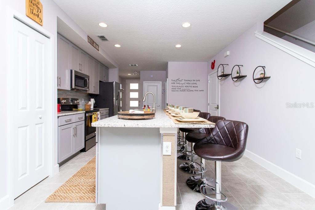 A kitchen features a granite-topped island with bar seating, gray cabinetry, and light-colored tile flooring — 4711 TERRA ESMERALDA DRIVE, KISSIMMEE, FL
