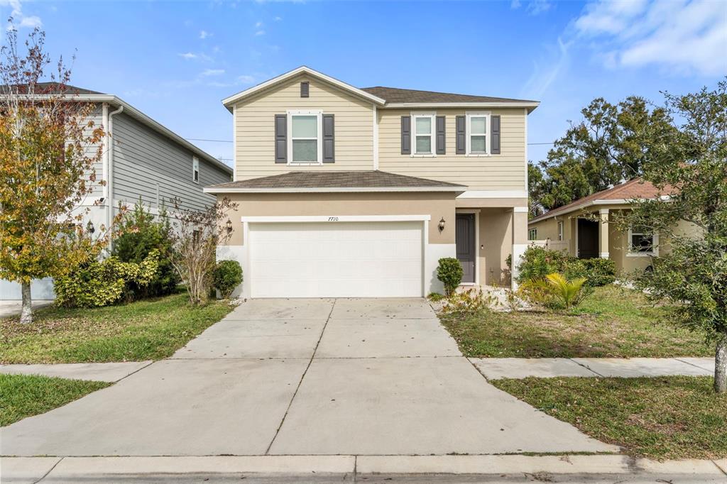 A two-story house with tan siding, a white garage door, and a concrete driveway — 7710 SUNSHINE BRIDGE AVE, GIBSONTON, FL