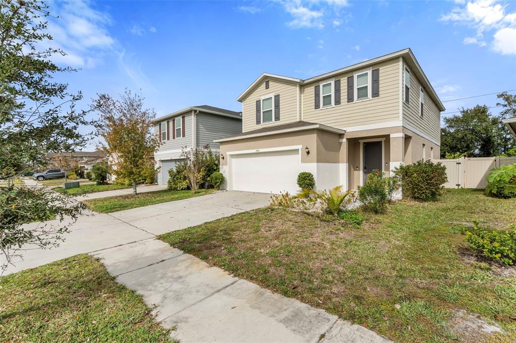 A two-story suburban house with beige siding, a white garage, and a concrete driveway — 7710 SUNSHINE BRIDGE AVE, GIBSONTON, FL