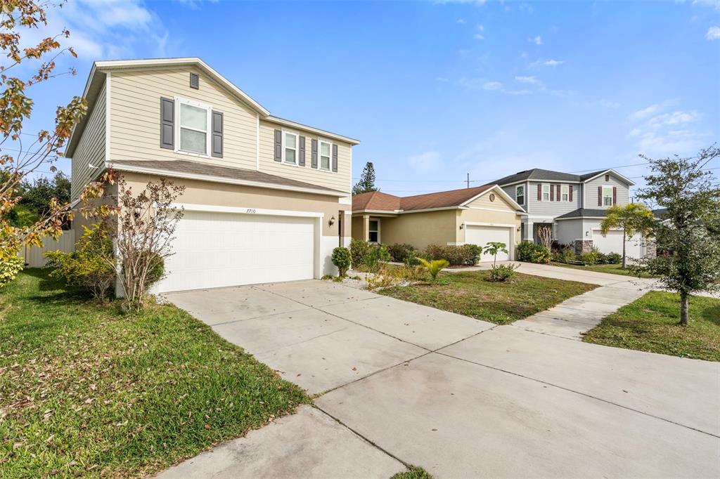 A two-story house with a beige exterior and a two-car garage sits on a street — 7710 SUNSHINE BRIDGE AVE, GIBSONTON, FL