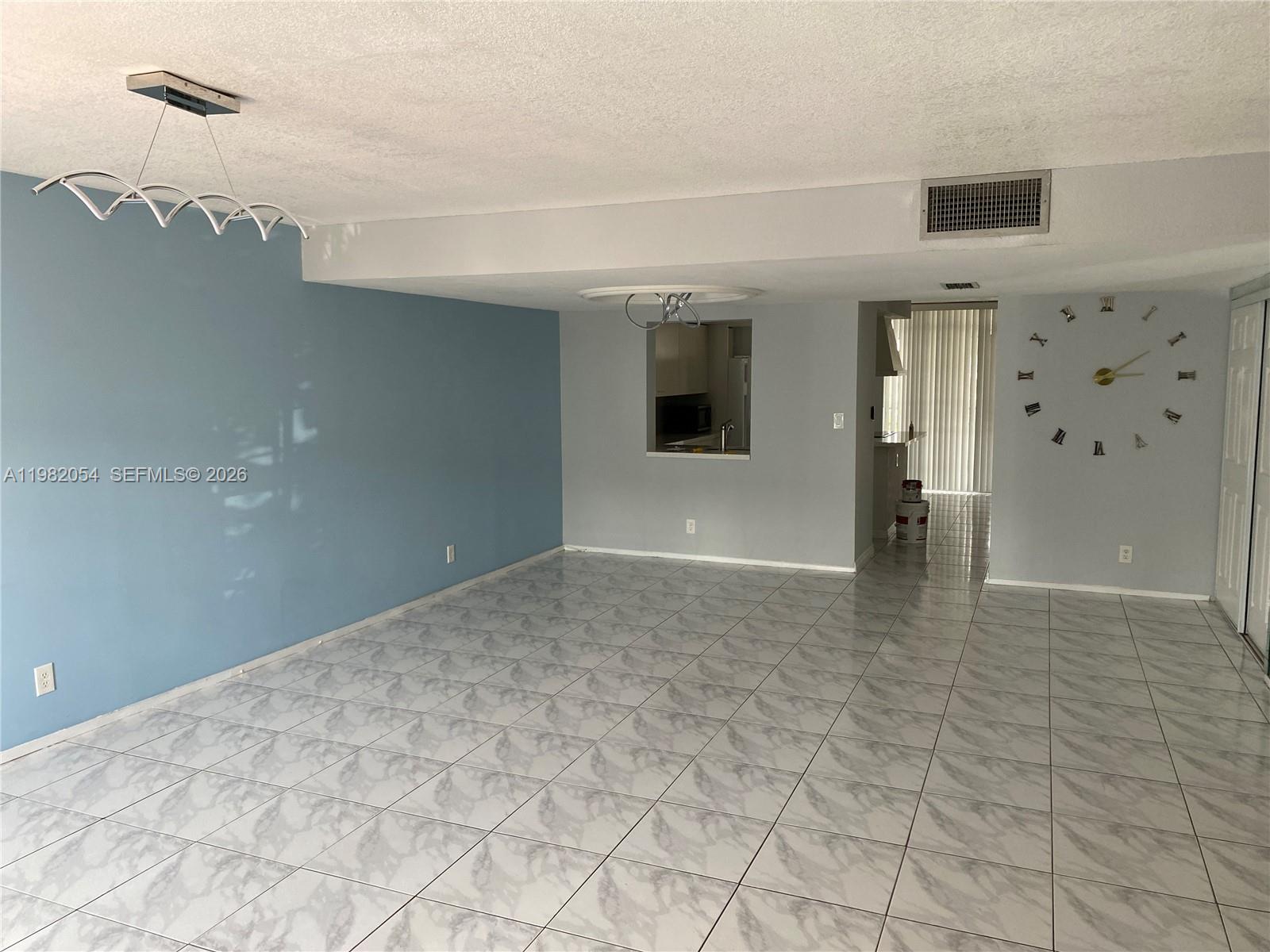 An empty room features blue and gray walls, marble-patterned tile flooring, and a wall clock — 802 NE 26th Ave # 802, Hallandale Beach FL 33009, HALLANDALE BEACH, FL
