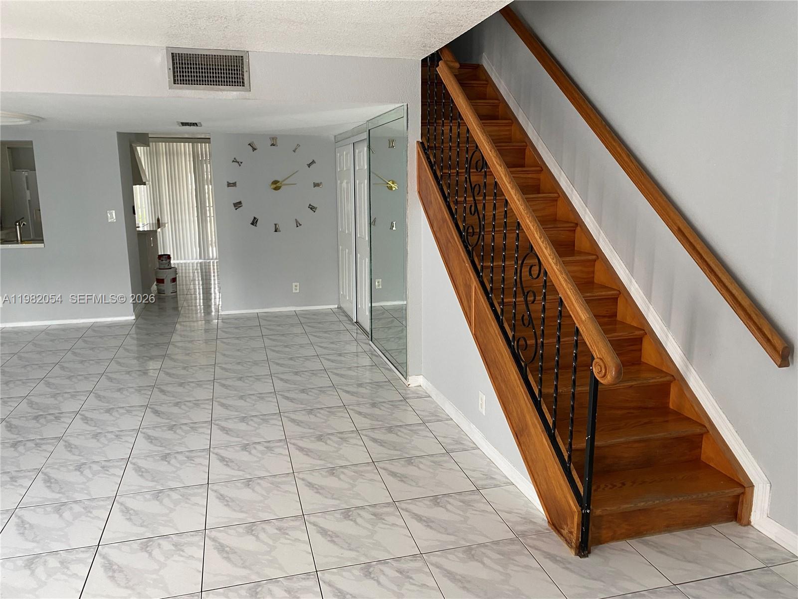 A room with light gray marble-patterned tile floors, a wooden staircase, and a wall clock — 802 NE 26th Ave # 802, Hallandale Beach FL 33009, HALLANDALE BEACH, FL