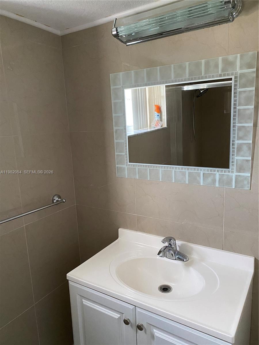 A bathroom features a white vanity, a tiled wall, and a rectangular mirror — 802 NE 26th Ave # 802, Hallandale Beach FL 33009, HALLANDALE BEACH, FL