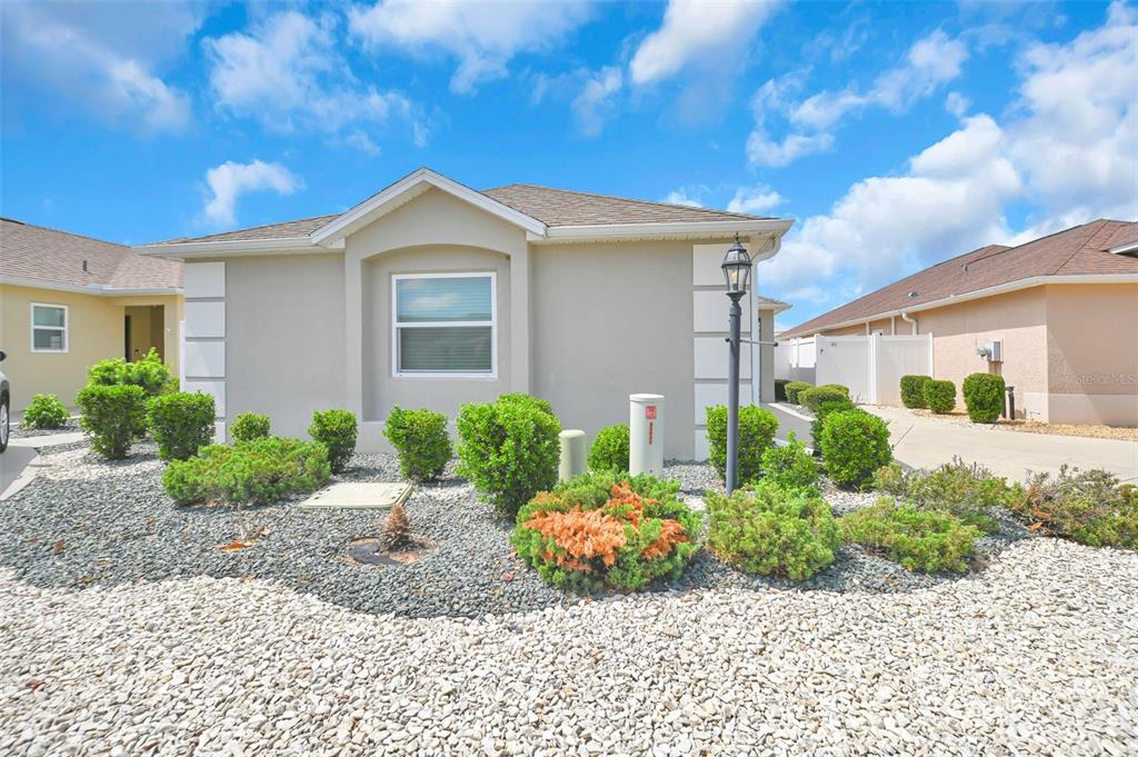 A single-story house with beige stucco siding and a gravel front yard with shrubs — 9188 SE 166TH SPRUNG LANE, THE VILLAGES, FL