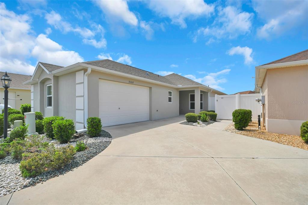 A beige single-story house features a two-car garage, a concrete driveway, and landscaped shrubs — 9188 SE 166TH SPRUNG LANE, THE VILLAGES, FL