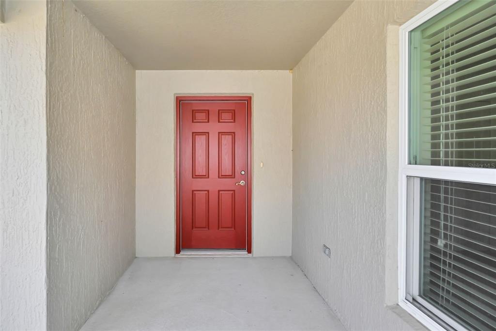 A red front door is centered on a covered porch next to a window — 9188 SE 166TH SPRUNG LANE, THE VILLAGES, FL