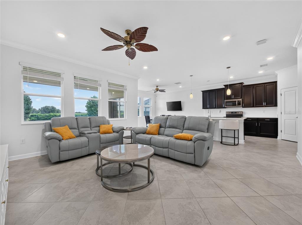 A living room with gray reclining sofas, a round coffee table, and an open kitchen — 8813 BETH PAGE LANE, DAVENPORT, FL