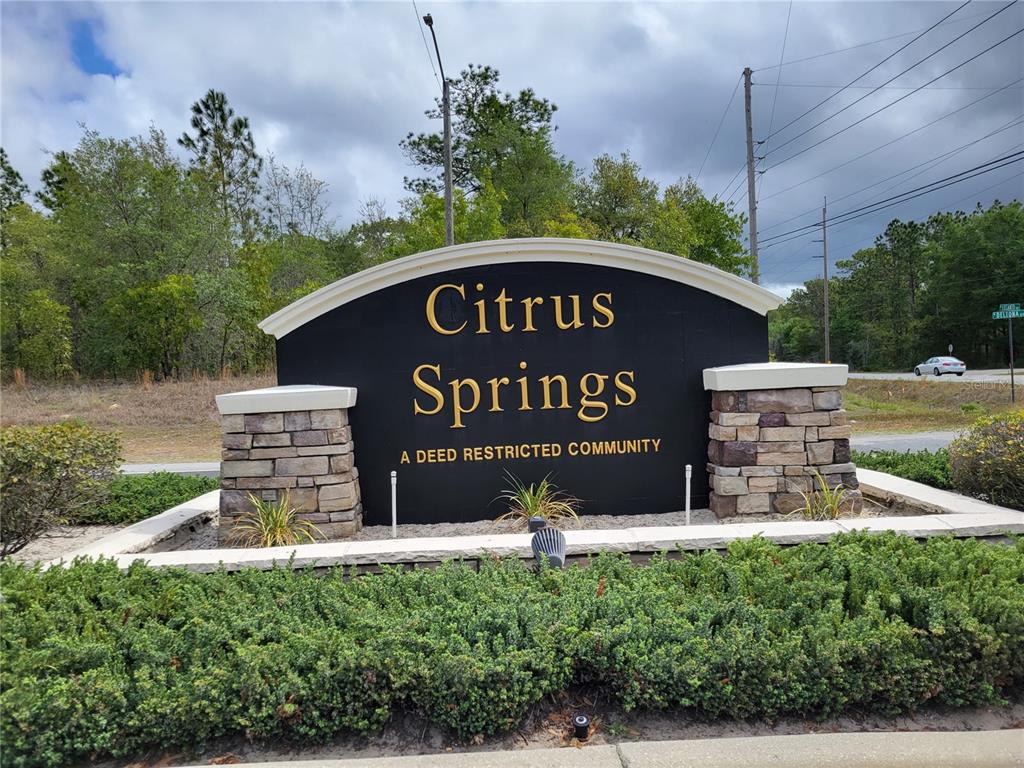 A black community entrance sign with stone pillars stands in front of trees and greenery — 9223 N BERTIN DRIVE, CITRUS SPRINGS, FL
