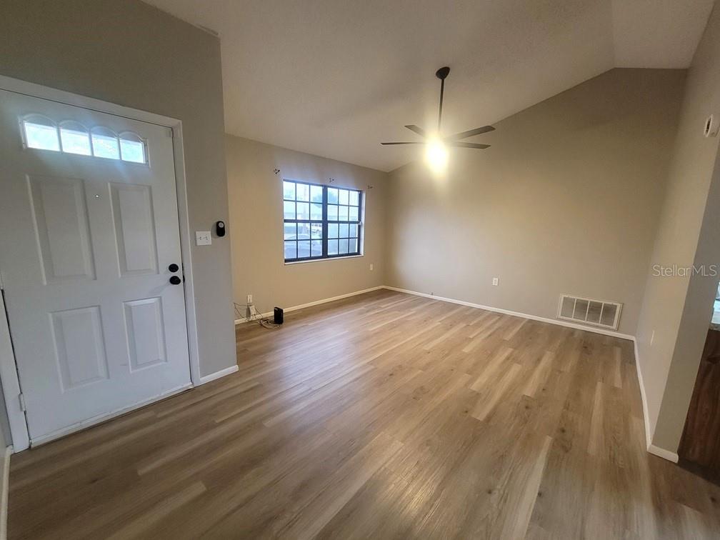 An empty room with light wood-look flooring, a ceiling fan, and a front door — 1305 CALAMONDIN DRIVE, HOLIDAY, FL