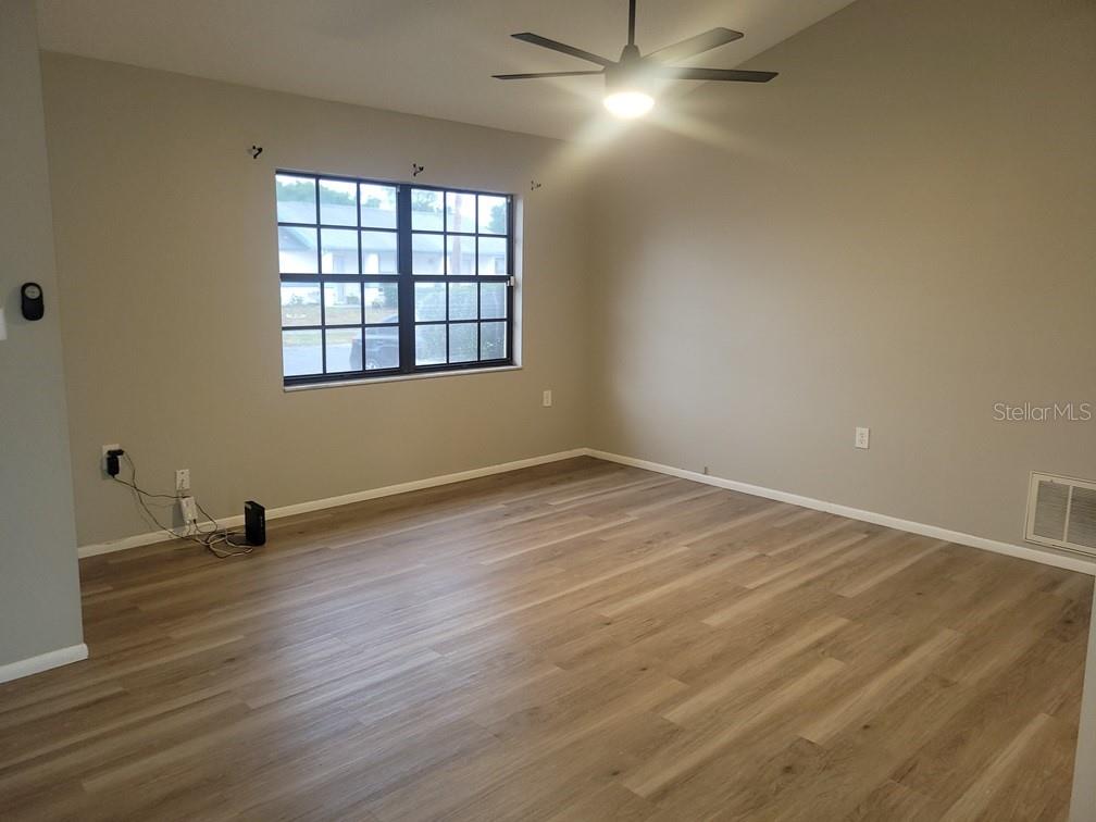 An empty living room features light wood-look flooring, beige walls, and a ceiling fan — 1305 CALAMONDIN DRIVE, HOLIDAY, FL