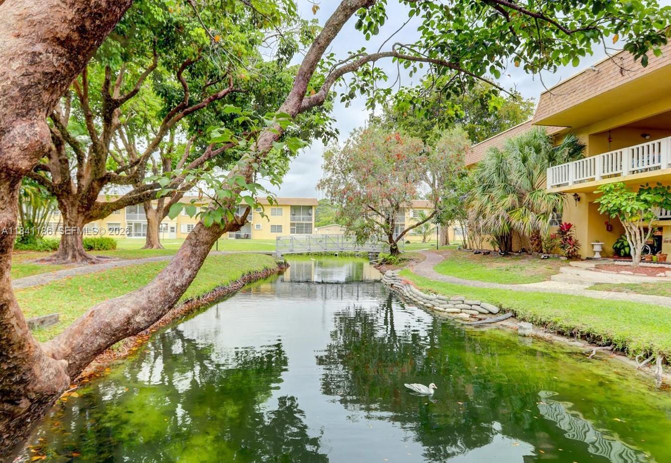 An outdoor swimming pool surrounded by a white fence, patio pavers, and lush palm trees — 5160 SW 40th Ave # 26D, Dania Beach FL 33314, DANIA BEACH, FL