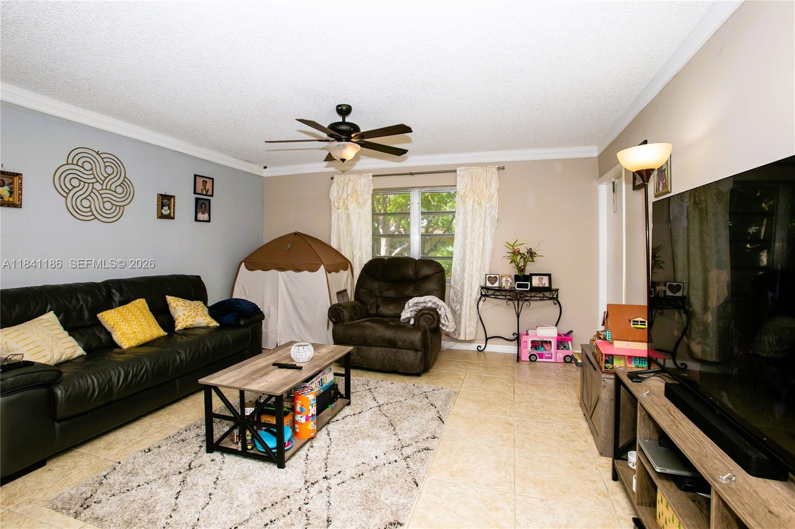An empty room features white walls, beige tile flooring, a ceiling fan, and a chandelier — 5160 SW 40th Ave # 26D, Dania Beach FL 33314, DANIA BEACH, FL