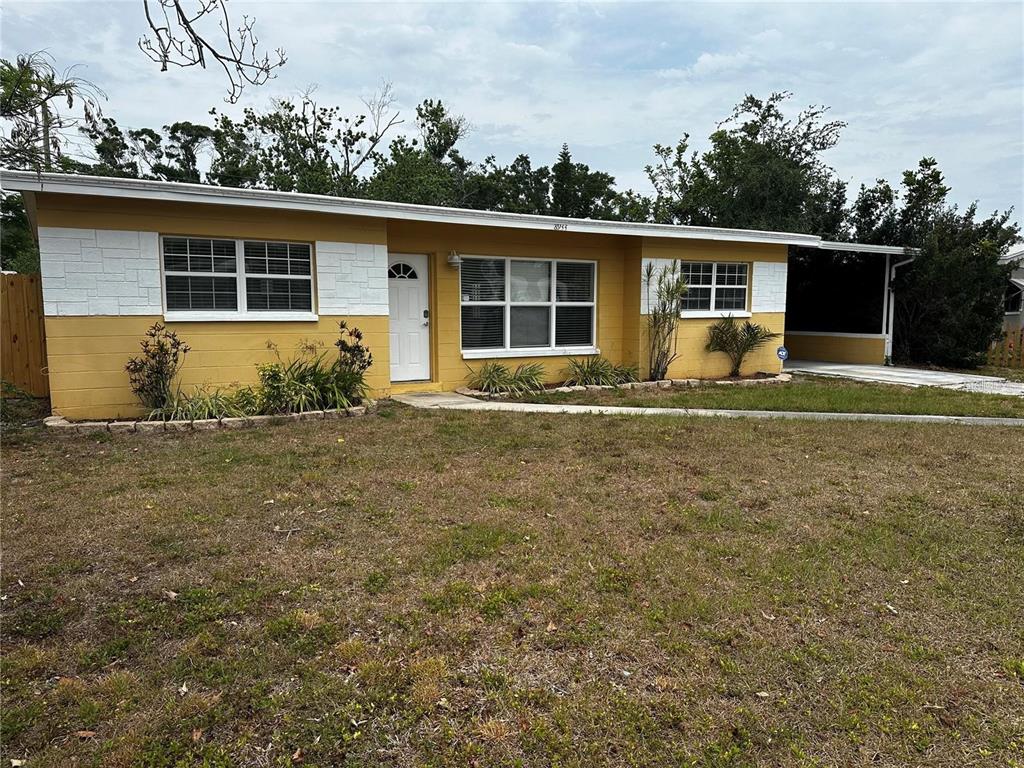 A yellow single-story house with white trim and a carport sits behind a grassy yard — 8933 NARCISSUS AVENUE, SEMINOLE, FL