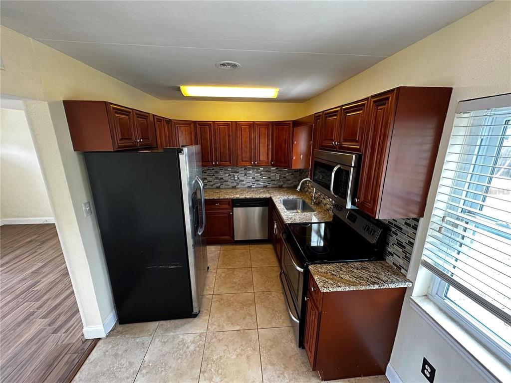 A kitchen features dark wood cabinets, granite countertops, stainless steel appliances, and tile flooring — 8933 NARCISSUS AVENUE, SEMINOLE, FL