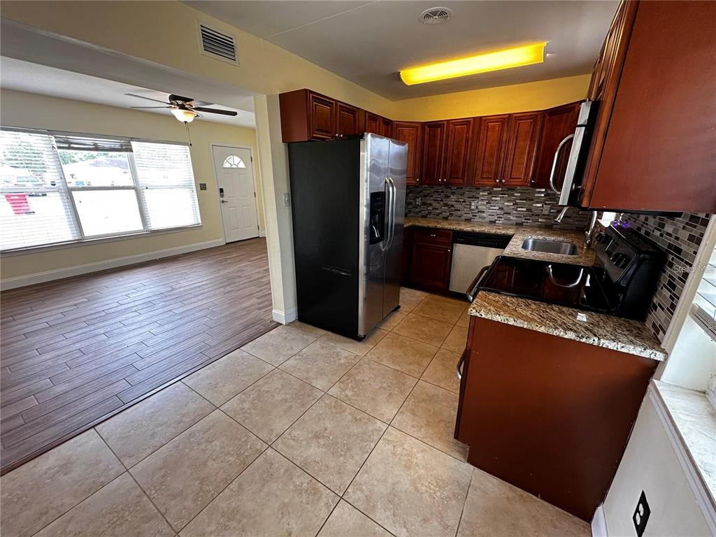 A kitchen with dark wood cabinets, granite countertops, and tile flooring opens to a living area — 8933 NARCISSUS AVENUE, SEMINOLE, FL