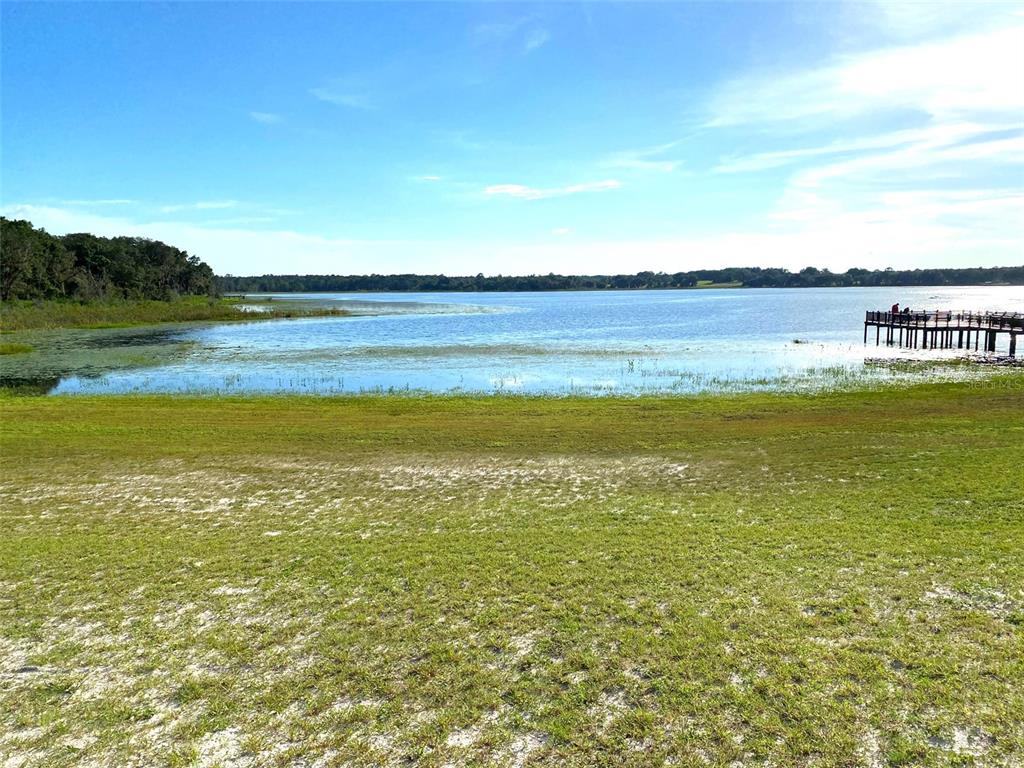 A grassy lawn leads to a lake with a wooden dock on the right — Lots 11.12 SW SHOREWOOD DRIVE, DUNNELLON, FL