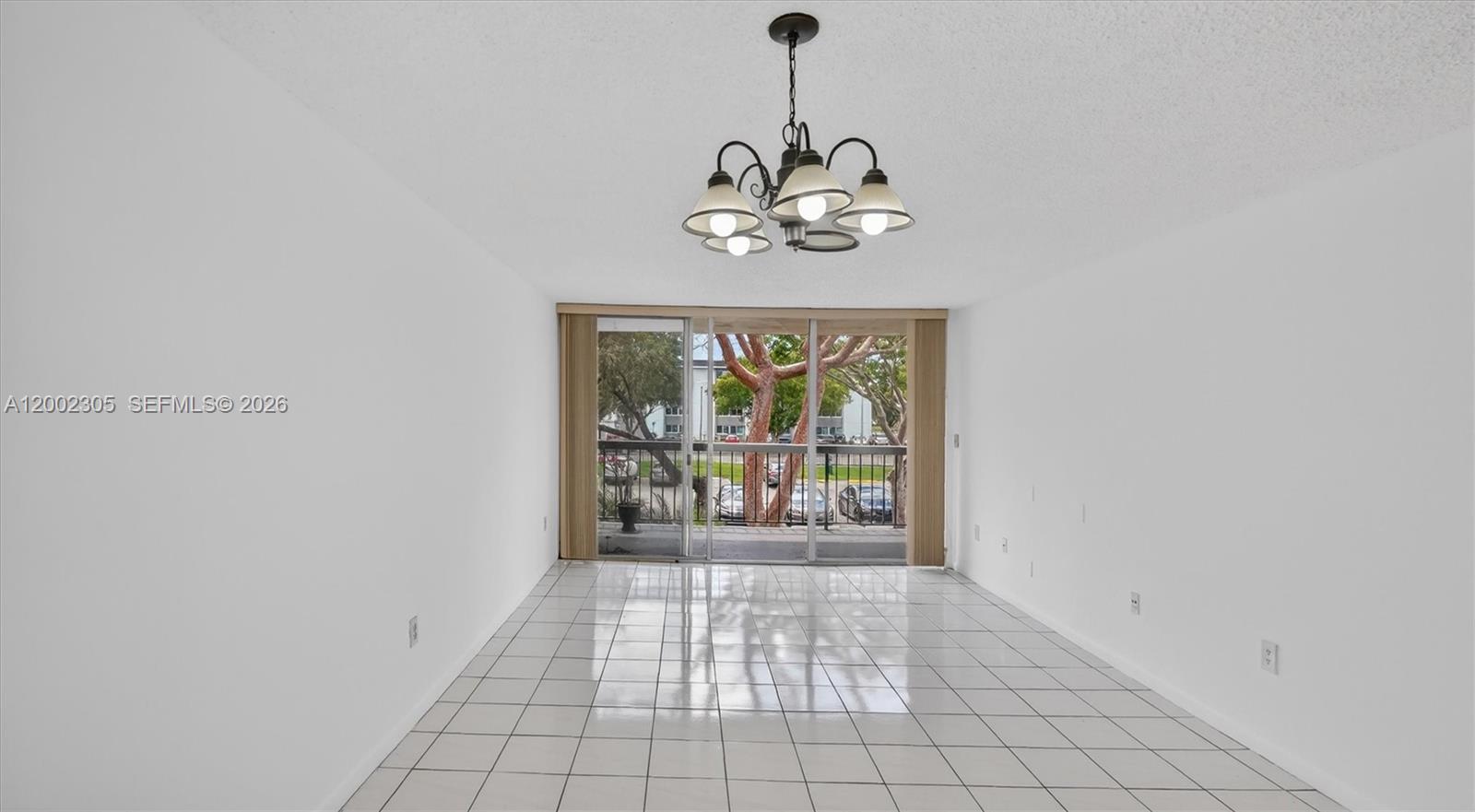 A bright dining room features white tile flooring, a chandelier, and a sliding glass door — 10975 SW 107th ST. # 202, Kendall FL 33176, KENDALL, FL