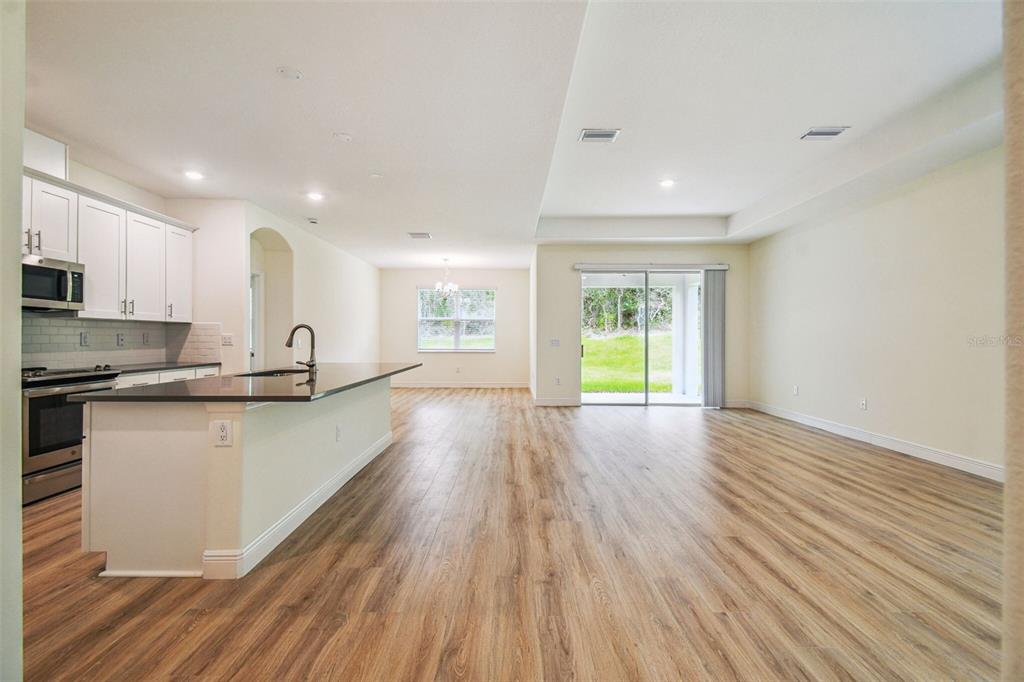 An open-concept kitchen and living area featuring white cabinets, dark countertops, and wood-look flooring — 11347 STRIPED BASS COURT, NEW PORT RICHEY, FL
