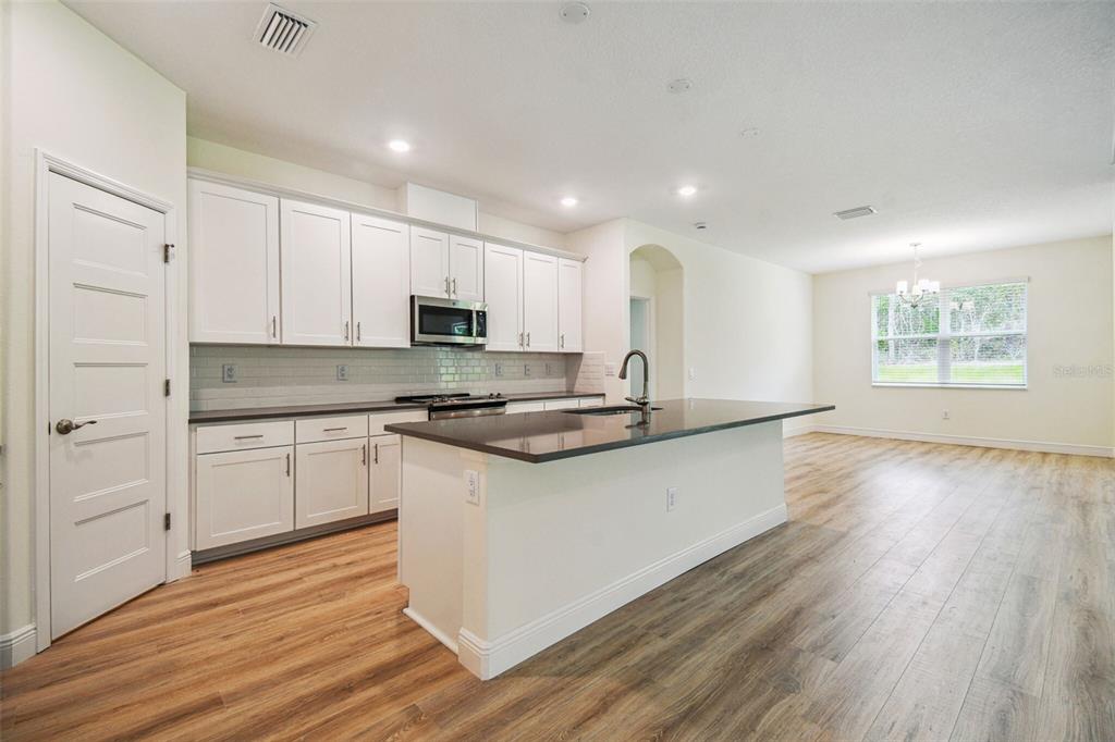 A modern kitchen features white cabinets, dark countertops, a central island, and light wood flooring — 11347 STRIPED BASS COURT, NEW PORT RICHEY, FL