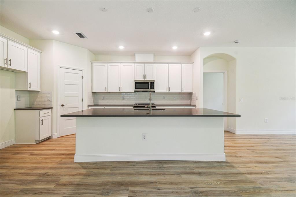 A kitchen with white cabinets, a dark island countertop, and light wood-look flooring — 11347 STRIPED BASS COURT, NEW PORT RICHEY, FL