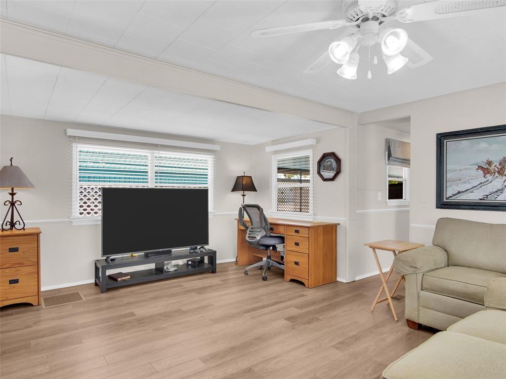 A living room features light wood flooring, a television on a stand, and a desk — 800 CHESAPEAKE DRIVE UNIT 55, TARPON SPRINGS, FL
