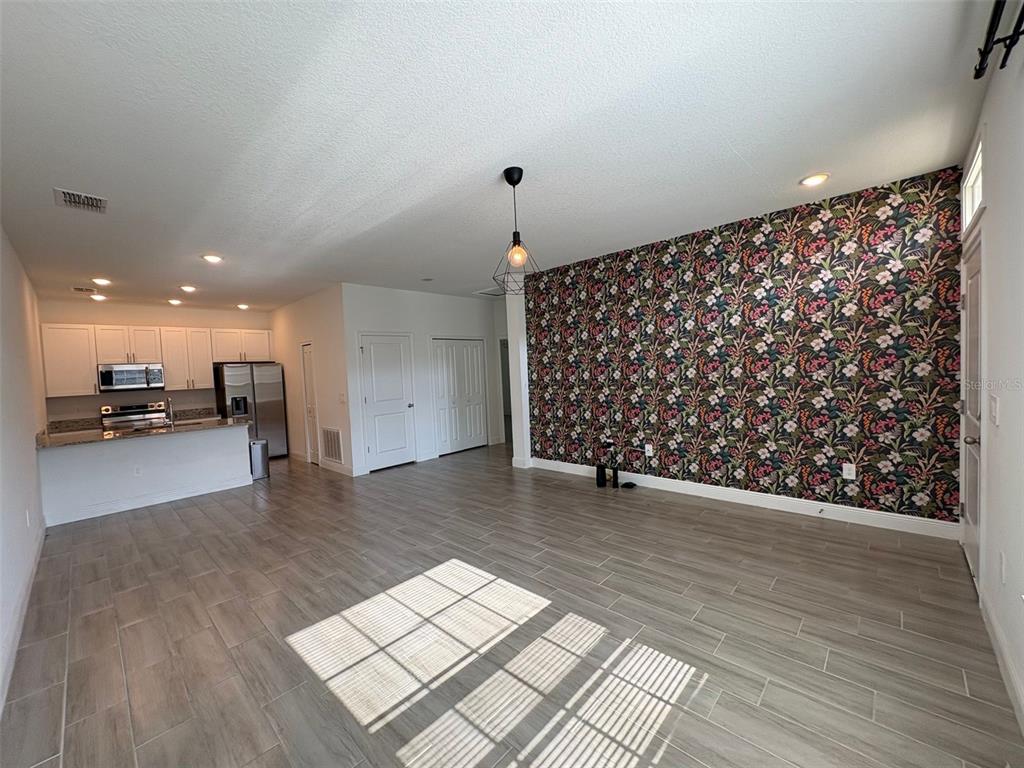 An open-concept living area features wood-look tile flooring and a floral accent wall — 1552 CUMIN DRIVE, POINCIANA, FL