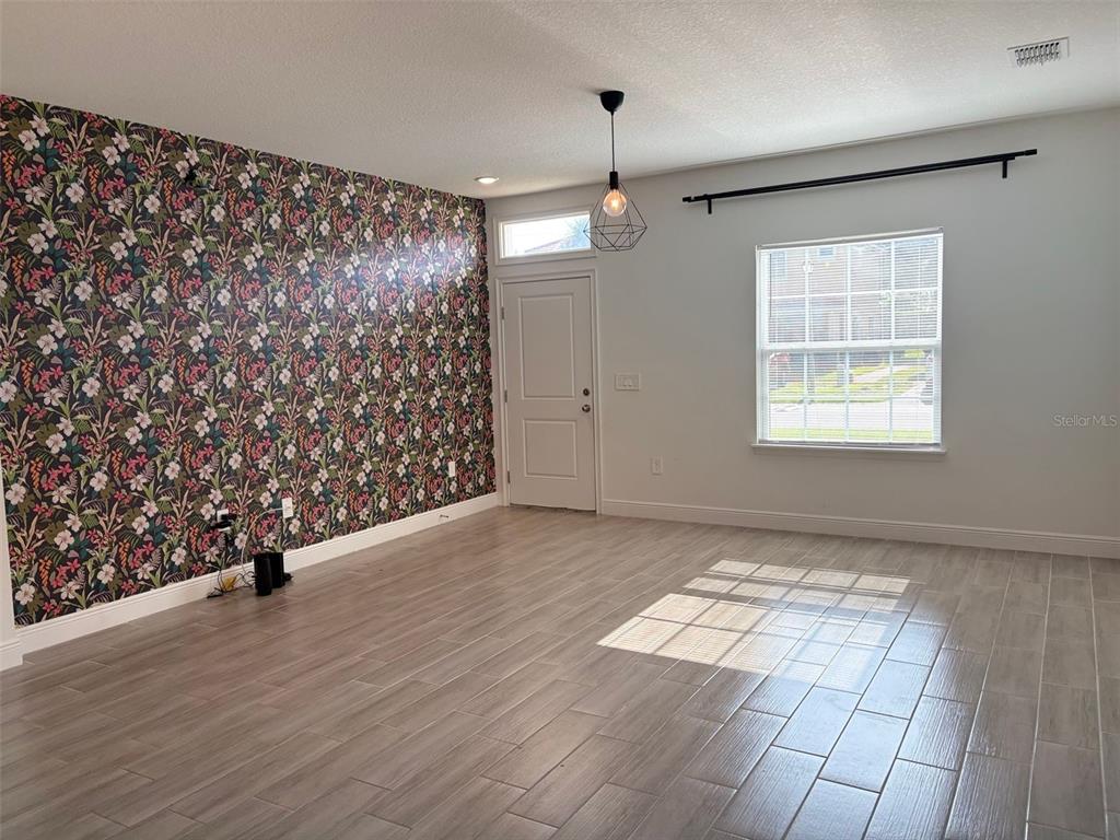 A room features wood-look tile flooring, a floral accent wall, and a single pendant light — 1552 CUMIN DRIVE, POINCIANA, FL