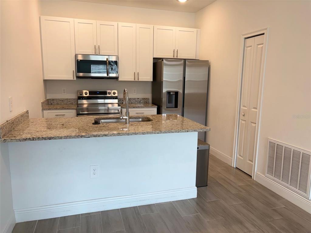 A kitchen with white cabinets, granite countertops, stainless steel appliances, and light wood-look flooring — 1552 CUMIN DRIVE, POINCIANA, FL
