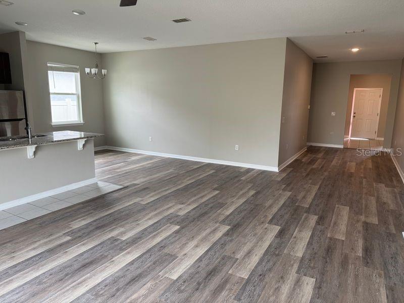 An open-concept living area features wood-look flooring, neutral walls, and a kitchen island — 3345 CURLEW AVENUE, LEESBURG, FL