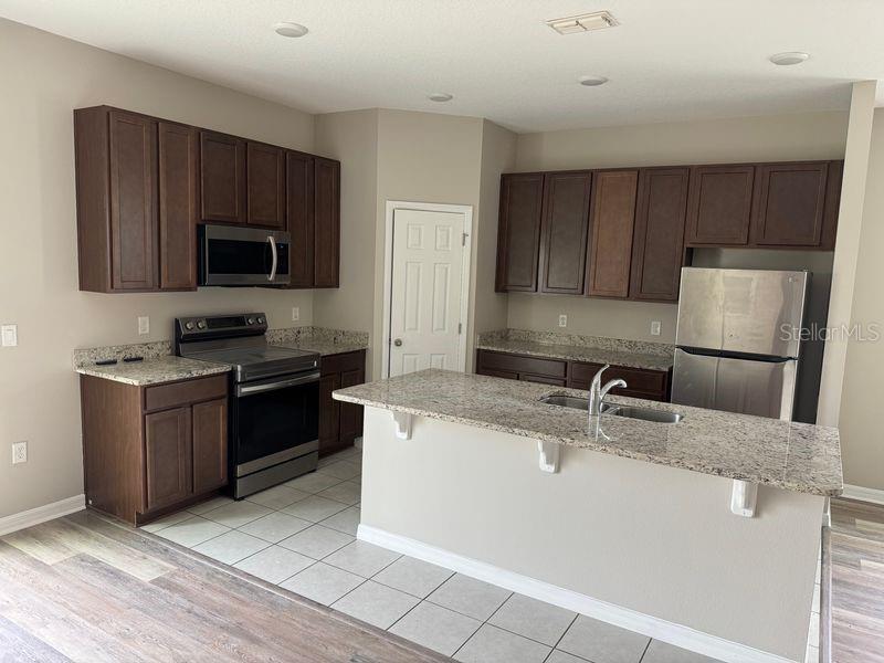 A kitchen features dark wood cabinets, granite countertops, stainless steel appliances, and a central island — 3345 CURLEW AVENUE, LEESBURG, FL