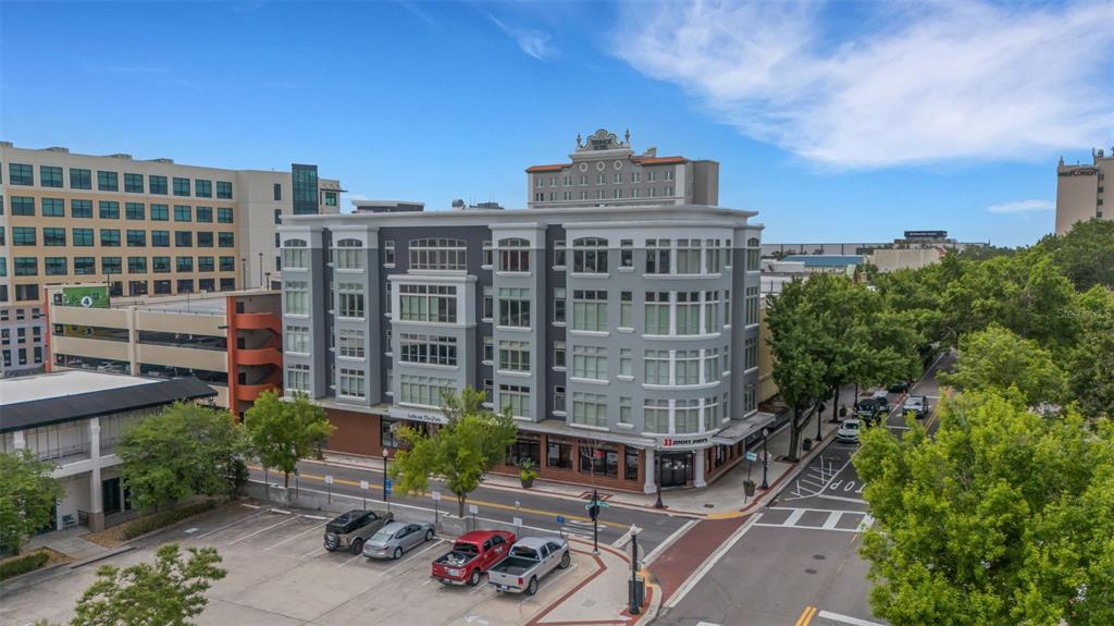 An aerial view shows a multi-story gray apartment building with ground-floor retail and street parking — 125 N KENTUCKY AVENUE UNIT 303, LAKELAND, FL